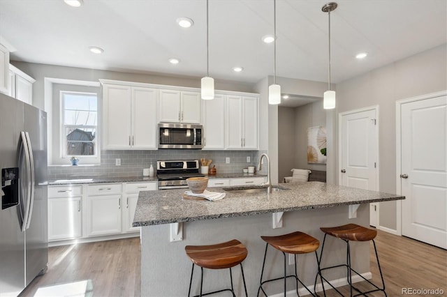 kitchen featuring backsplash, appliances with stainless steel finishes, a sink, light wood-type flooring, and a kitchen breakfast bar