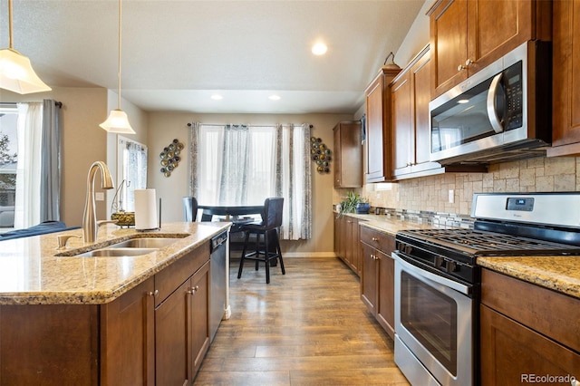 kitchen featuring hardwood / wood-style floors, a kitchen island with sink, sink, hanging light fixtures, and stainless steel appliances