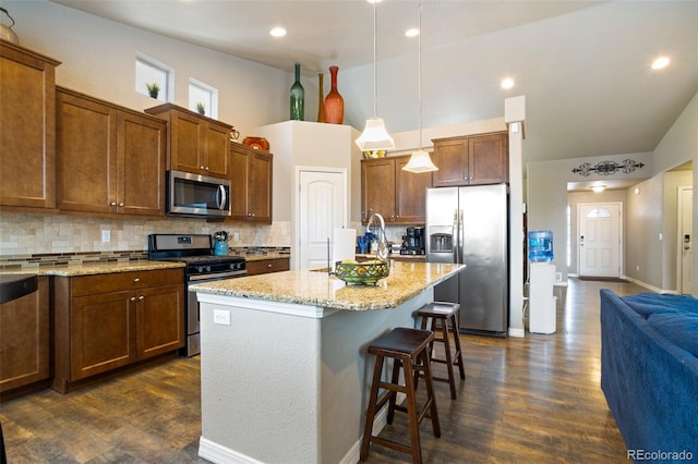 kitchen featuring a kitchen island with sink, hanging light fixtures, appliances with stainless steel finishes, and dark wood-type flooring