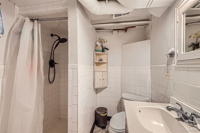 bathroom featuring a sink, tile walls, toilet, a stall shower, and wainscoting