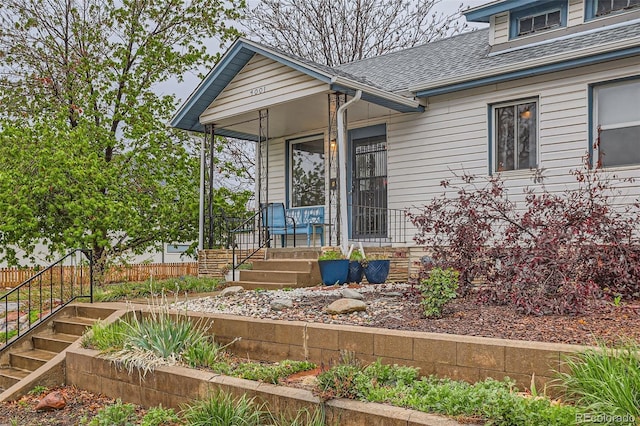 property entrance featuring a porch, a shingled roof, and fence