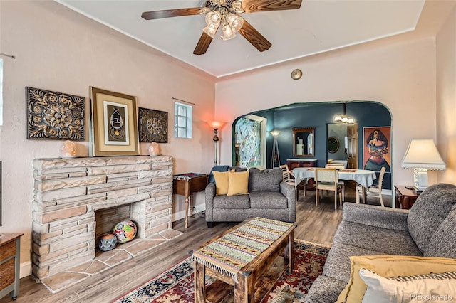 living room featuring wood finished floors, ceiling fan, arched walkways, and a fireplace