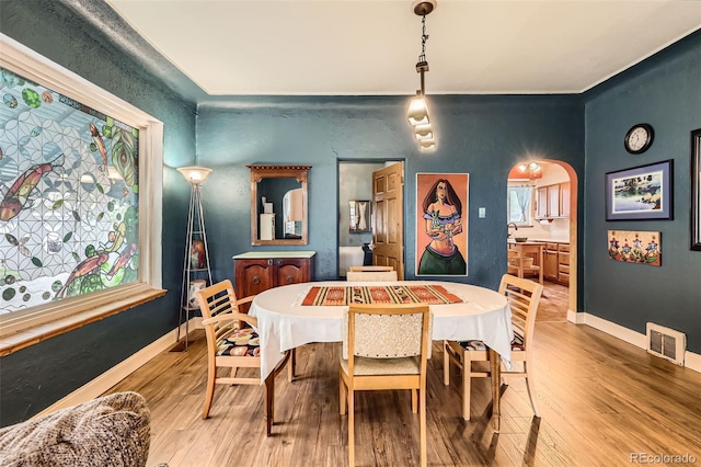 dining area featuring arched walkways, light wood finished floors, baseboards, and a textured wall
