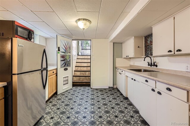 kitchen featuring freestanding refrigerator, a sink, light countertops, and white cabinets