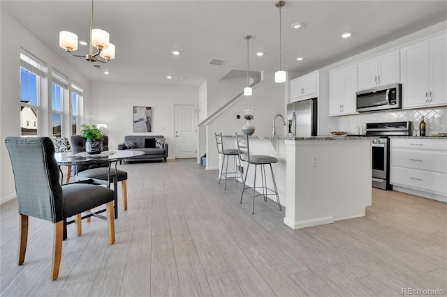 kitchen with decorative light fixtures, a center island with sink, white cabinetry, appliances with stainless steel finishes, and light wood-type flooring