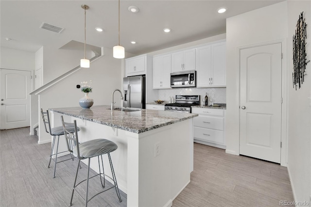 kitchen with white cabinetry, stone counters, a center island with sink, appliances with stainless steel finishes, and decorative light fixtures