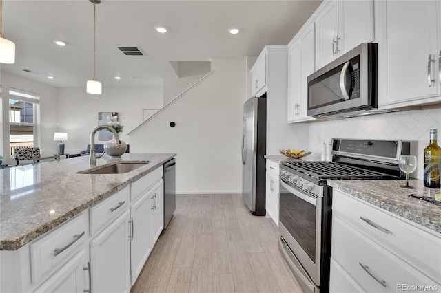 kitchen with hanging light fixtures, sink, white cabinetry, appliances with stainless steel finishes, and light hardwood / wood-style floors