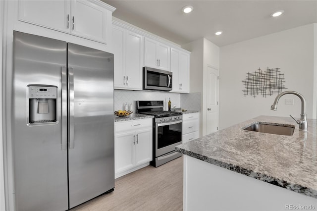 kitchen with light wood-type flooring, sink, white cabinets, stainless steel appliances, and light stone countertops