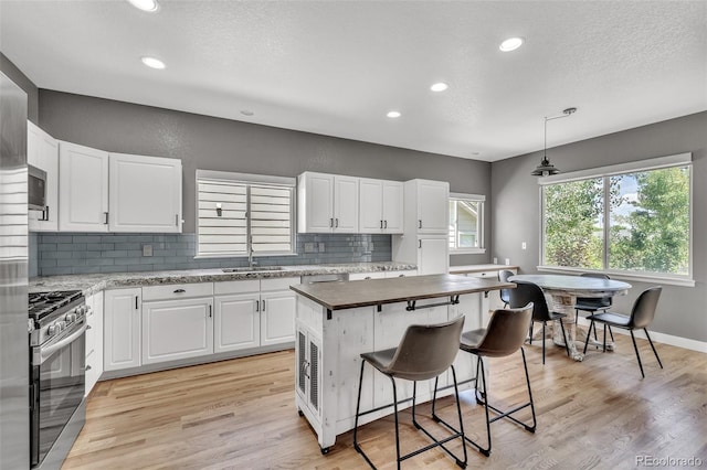 750 Deer Clover Cir, Castle Pines, CO 80108 - kitchen featuring gas stove, decorative backsplash, white cabinets, a breakfast bar, and light wood-type flooring
