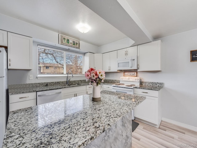 kitchen with light stone counters, white appliances, white cabinetry, and a sink