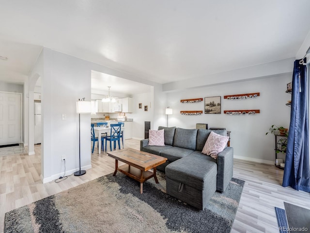 living room featuring light wood finished floors, baseboards, arched walkways, and an inviting chandelier