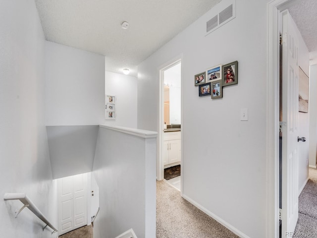 hall with a textured ceiling, carpet floors, an upstairs landing, and visible vents