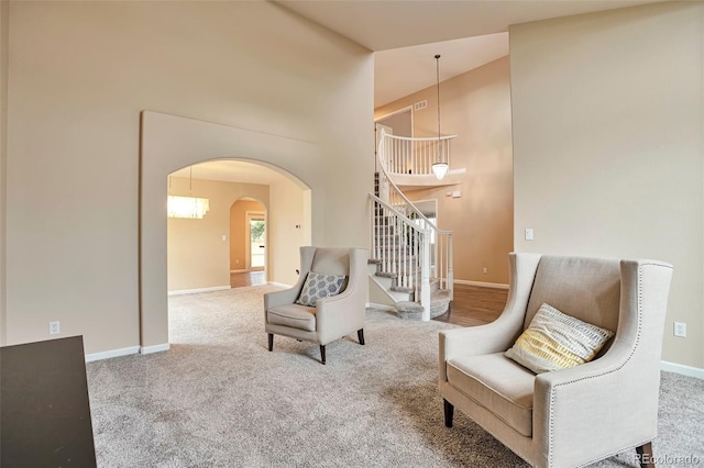 sitting room featuring carpet flooring, a high ceiling, arched walkways, stairs, and baseboards