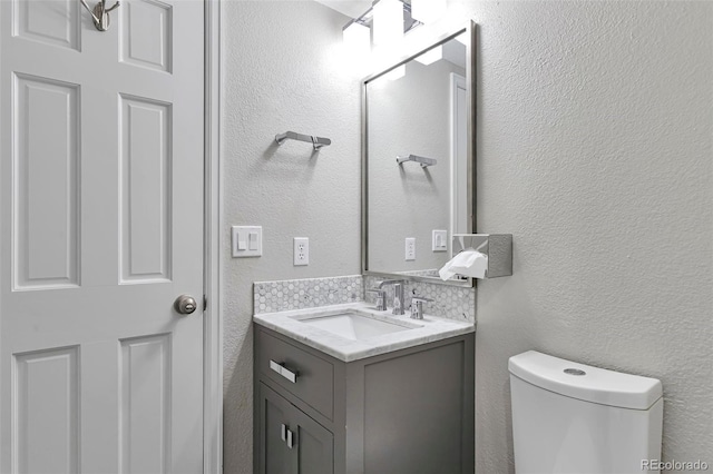 half bath with toilet, a textured wall, and vanity