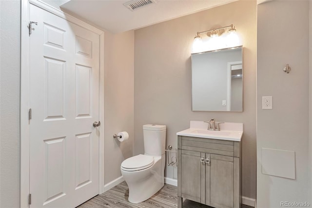 bathroom featuring vanity, toilet, baseboards, wood finished floors, and visible vents