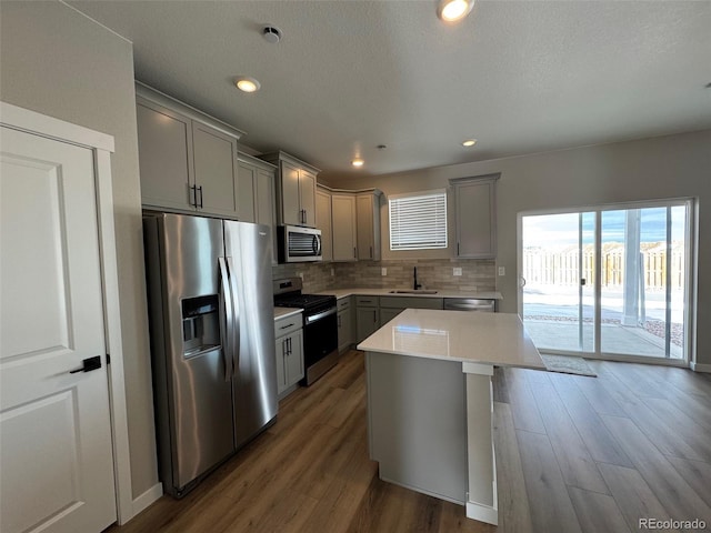kitchen with wood finished floors, gray cabinetry, light countertops, appliances with stainless steel finishes, and backsplash