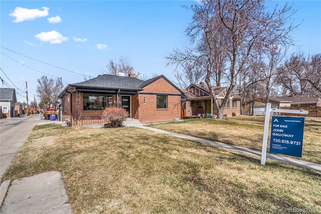 view of front of property featuring a front yard, brick siding, roof with shingles, and a chimney