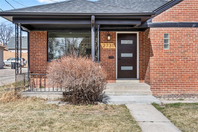 view of exterior entry with brick siding and roof with shingles