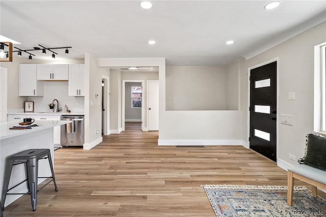 kitchen with dishwasher, light countertops, light wood-style flooring, white cabinets, and a sink