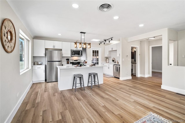 kitchen featuring visible vents, a breakfast bar, appliances with stainless steel finishes, white cabinets, and a sink