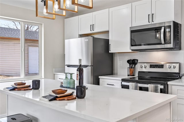 kitchen with decorative light fixtures, a center island, white cabinetry, stainless steel appliances, and light countertops