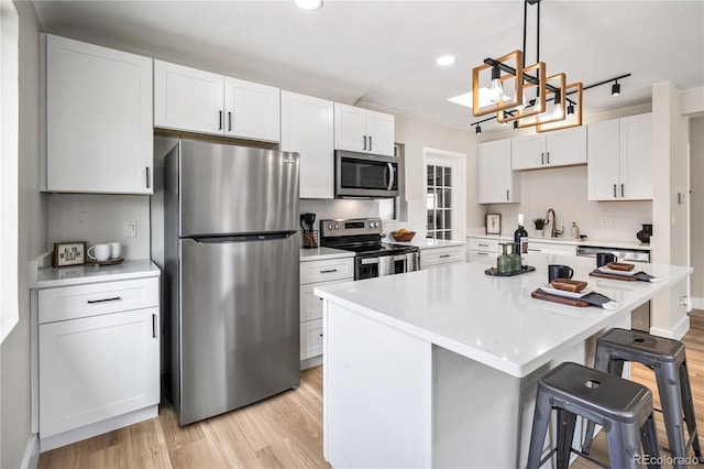 kitchen featuring a breakfast bar, light countertops, appliances with stainless steel finishes, white cabinetry, and light wood-type flooring