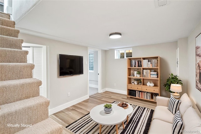 living room featuring light wood finished floors, visible vents, stairs, and baseboards