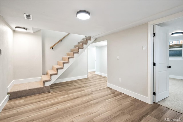 basement featuring visible vents, baseboards, light wood-style floors, and stairs