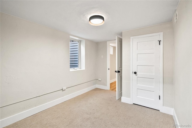 empty room featuring a textured ceiling, baseboards, and light carpet