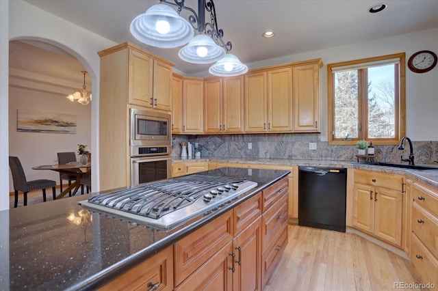 kitchen featuring stainless steel appliances, a sink, dark stone counters, tasteful backsplash, and light wood-style flooring