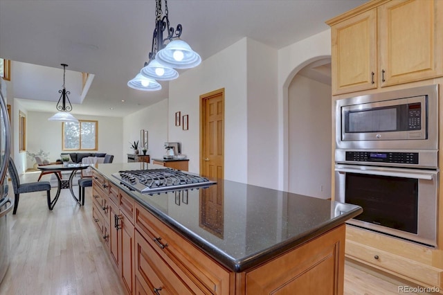 kitchen featuring stainless steel appliances, a center island, open floor plan, light wood-style flooring, and dark stone counters