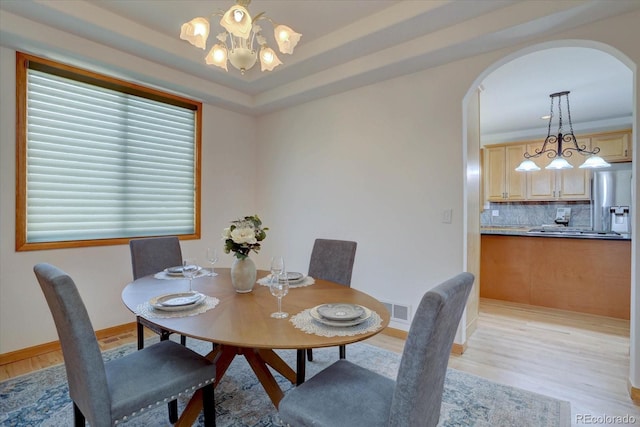 dining space featuring light wood finished floors, a chandelier, arched walkways, and baseboards