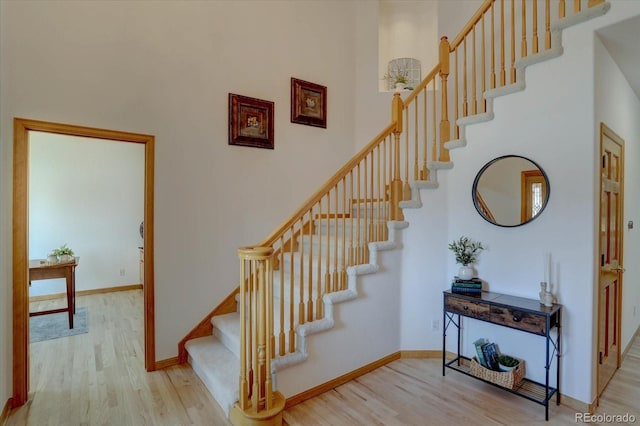 stairway with wood finished floors, baseboards, and a high ceiling