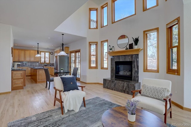 living area with baseboards, light wood-type flooring, a tiled fireplace, a high ceiling, and recessed lighting