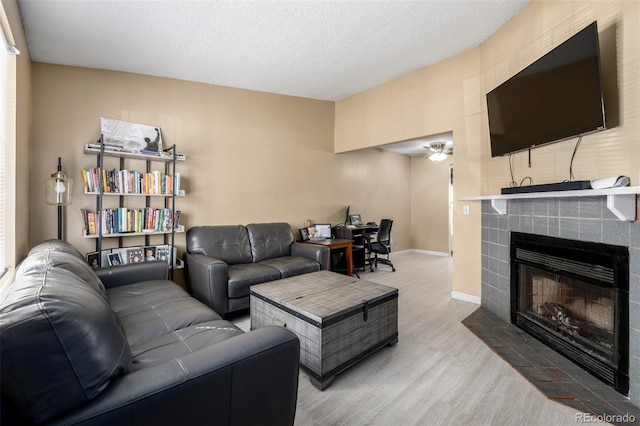 living area with light wood-style flooring, a fireplace, baseboards, and a textured ceiling