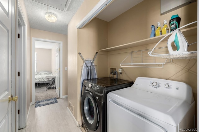 washroom featuring light wood-type flooring, a textured ceiling, attic access, laundry area, and washing machine and clothes dryer