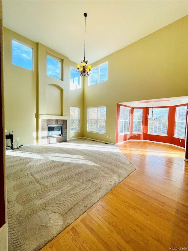 16866 E Peakview Ave, Aurora, CO 80016 - unfurnished living room featuring a chandelier, wood finished floors, a tiled fireplace, and a towering ceiling