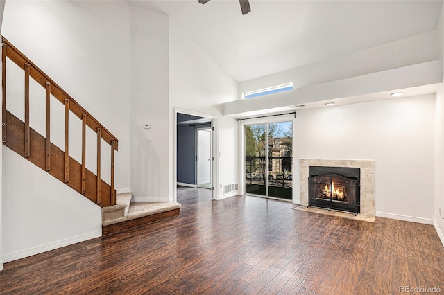 unfurnished living room with stairs, wood finished floors, a fireplace, baseboards, and a high ceiling
