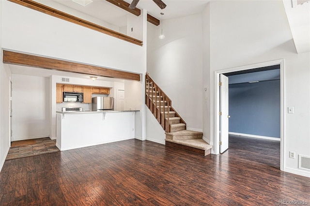 unfurnished living room featuring stairs, dark wood-type flooring, beam ceiling, a ceiling fan, and baseboards