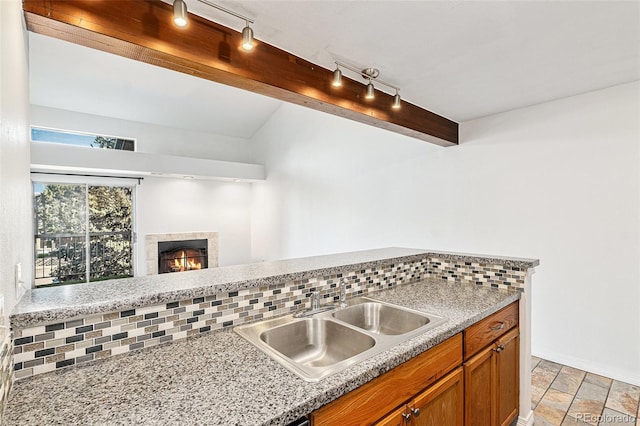 kitchen with a sink, backsplash, brown cabinets, and a tiled fireplace