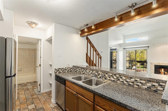 kitchen with stainless steel appliances, a sink, light stone finish flooring, dark countertops, and decorative backsplash