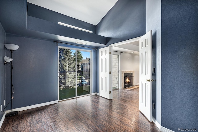 unfurnished room with wood finished floors, baseboards, a fireplace with flush hearth, and a textured wall