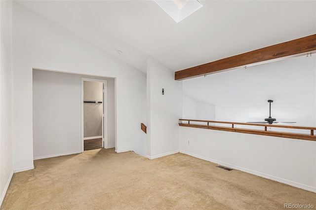 spare room featuring vaulted ceiling, light carpet, a ceiling fan, baseboards, and a skylight