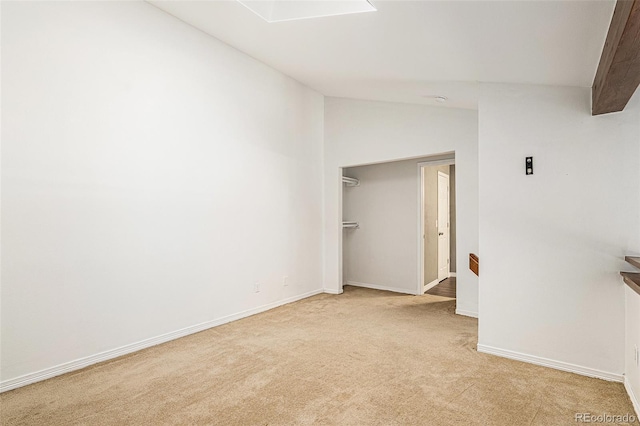 empty room featuring vaulted ceiling, light carpet, and baseboards