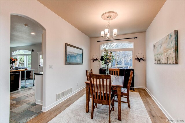 dining area featuring a chandelier, light wood-type flooring, arched walkways, and baseboards