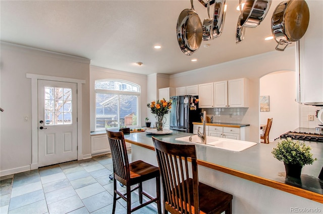 kitchen featuring freestanding refrigerator, a sink, decorative backsplash, a kitchen bar, and crown molding