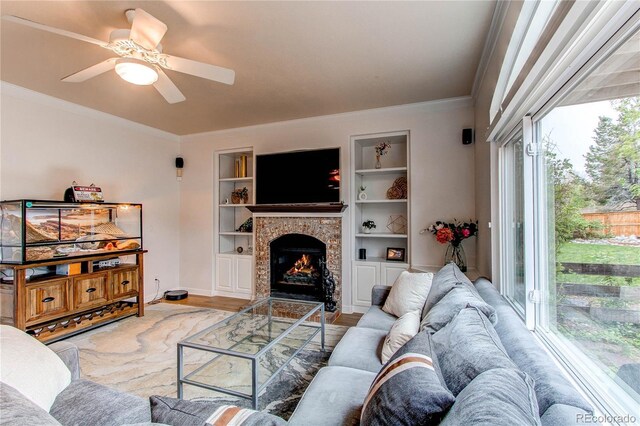 living area with crown molding, a ceiling fan, a fireplace with flush hearth, built in features, and wood finished floors