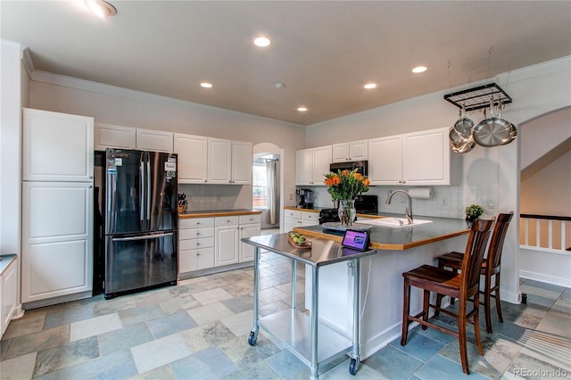 kitchen featuring freestanding refrigerator, tasteful backsplash, a breakfast bar area, a peninsula, and white cabinetry