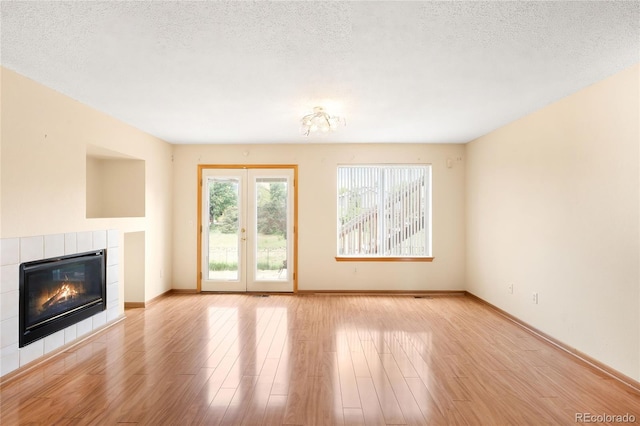 8879 Apache Plume Dr, Parker, CO 80134 - unfurnished living room featuring a tile fireplace, light wood finished floors, baseboards, a textured ceiling, and french doors