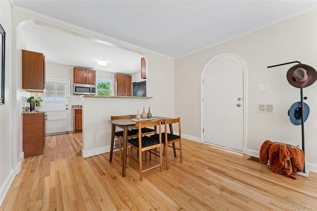 1691 Roslyn St, Denver, CO 80220 - dining area with arched walkways, light wood-style floors, crown molding, a textured ceiling, and baseboards